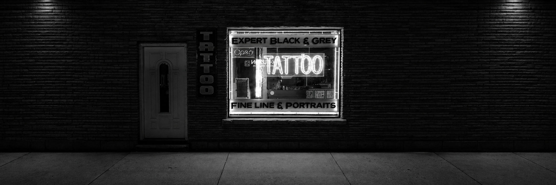 Black-and-white tattoo studio storefront with a neon tattoo sign